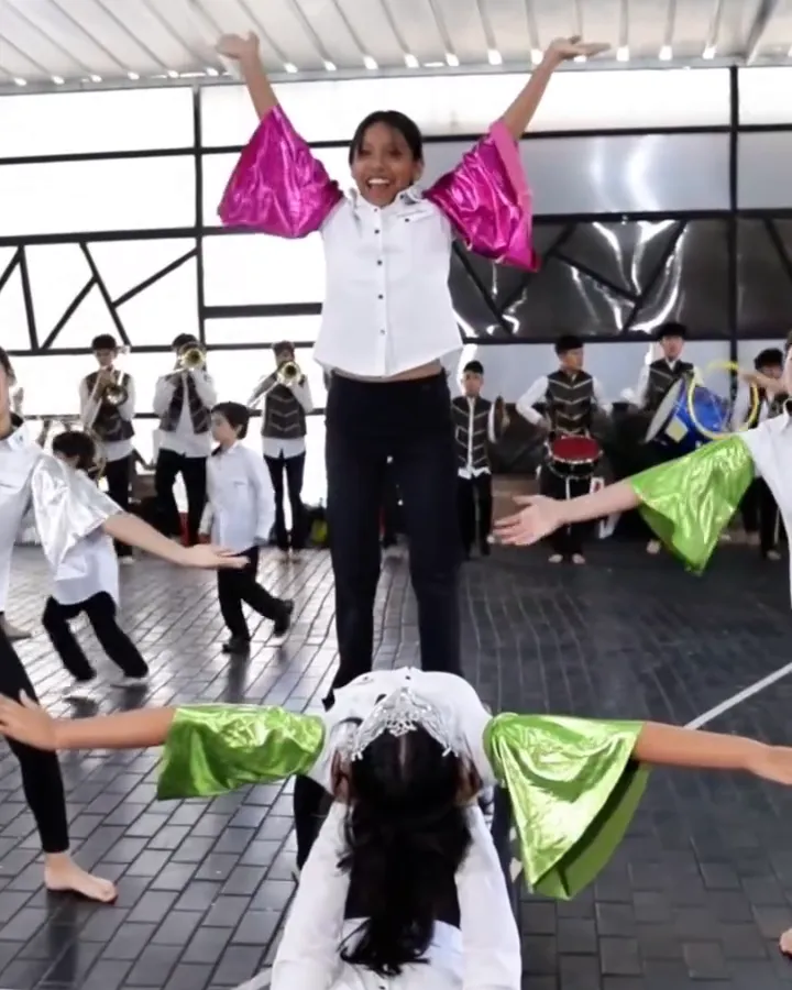 Alumna con la camisa del uniforme abre los brazos en V durante un ensayo