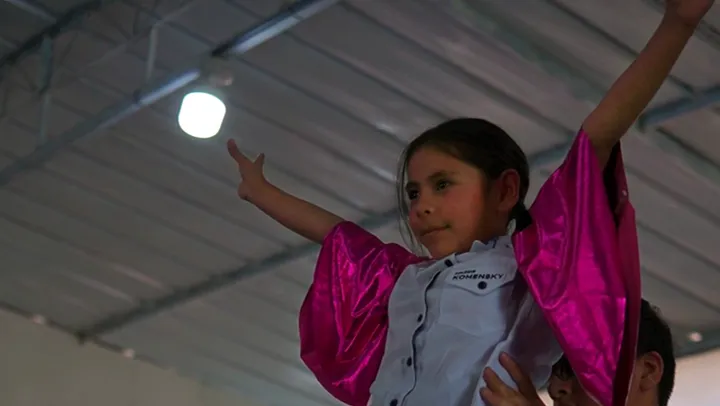 Alumna con mangas fucsia ensaya una danza con los brazos en alto