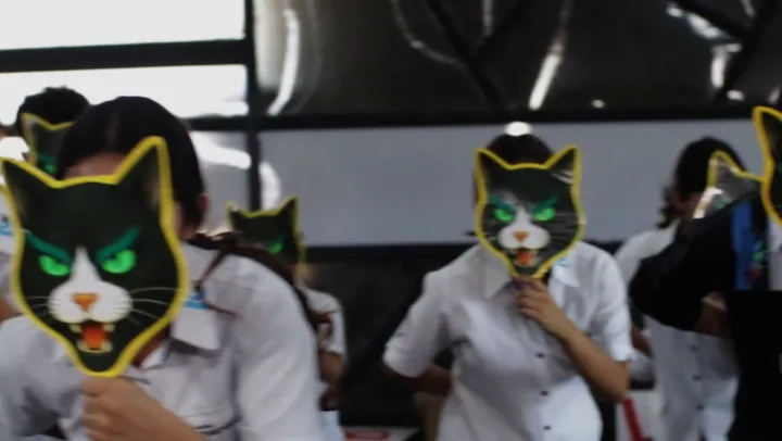 Alumnos con la camisa del uniforme ensayan con máscaras de gato