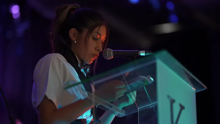 Alumna habla en el atril del colegio, con micrófono y luz de escenario